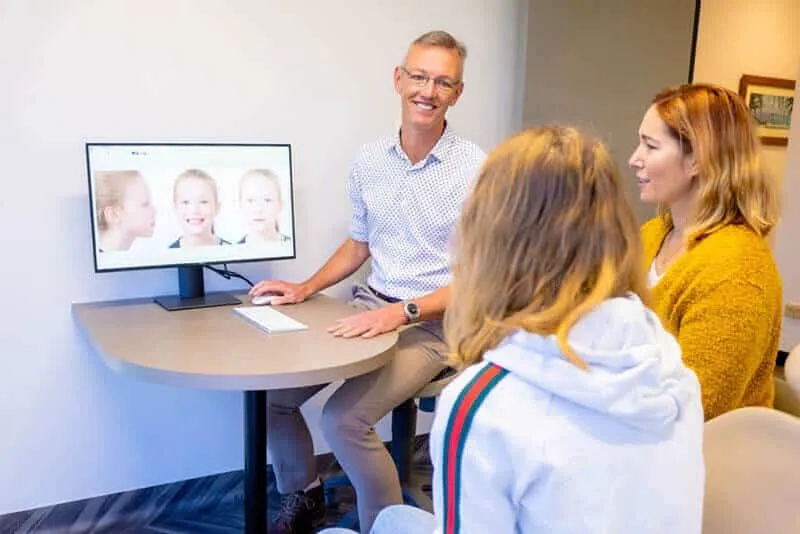 Orthodontist showing treatment images on a screen to a parent and a young patient
