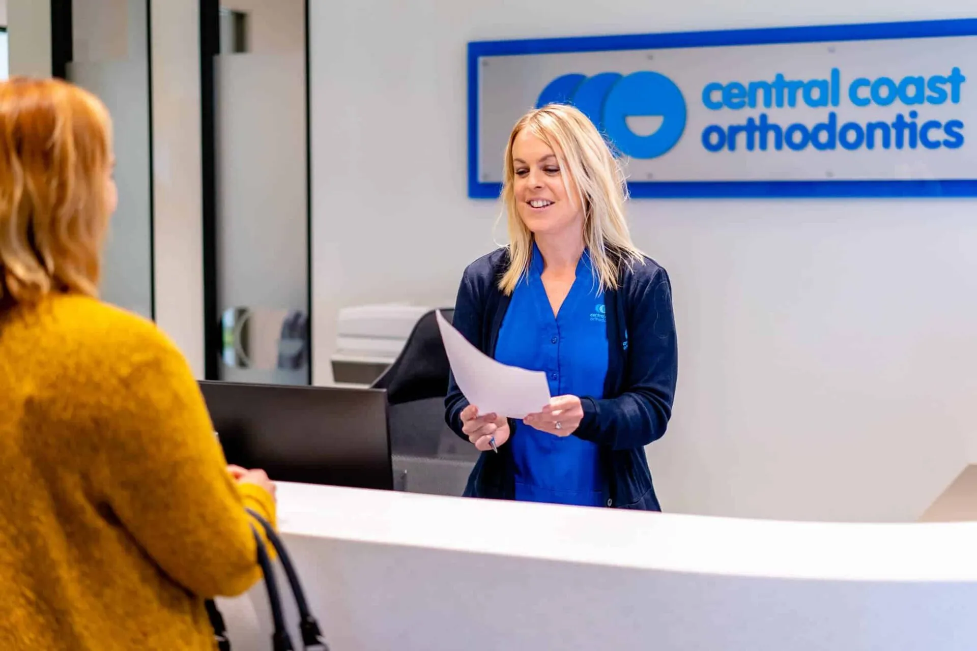 Receptionist handing paperwork to a patient at the Central Coast Orthodontics front desk