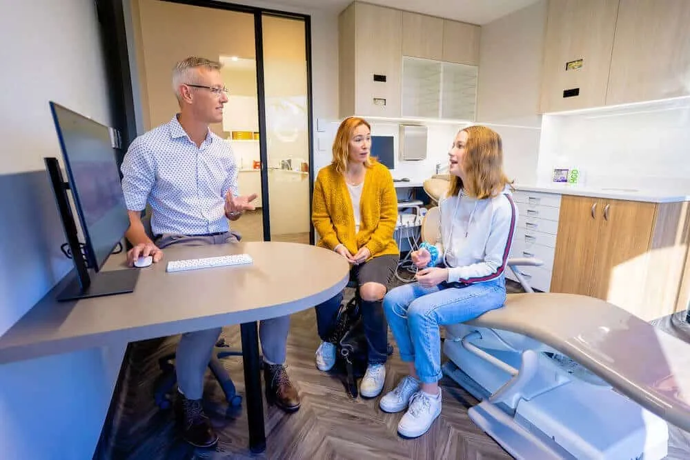 Orthodontist talking with a parent and a teenage patient in a consultation room