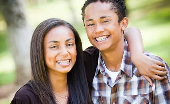 Two smiling teenagers outdoors, one with an arm around the other