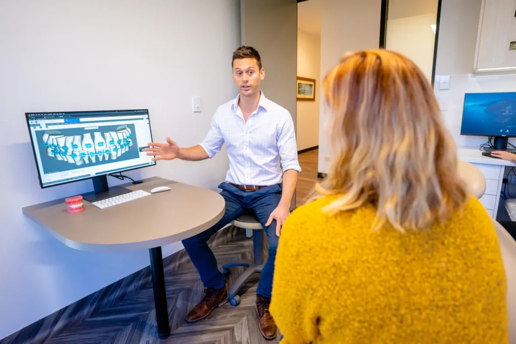 Orthodontist showing treatment images on a screen to a patient at a desk